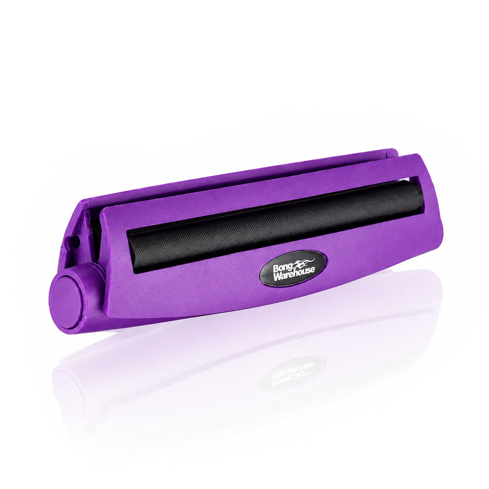 Purple king size 110mm plastic cigarette rolling machine from Bong Warehouse, angled view showing the black rolling apron and logo badge
