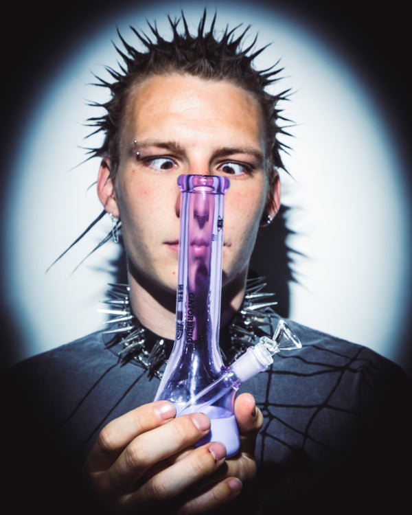 Man in the spotlight holding the purple Gatorbeug Mini Beaker Bong from Bong Warehouse