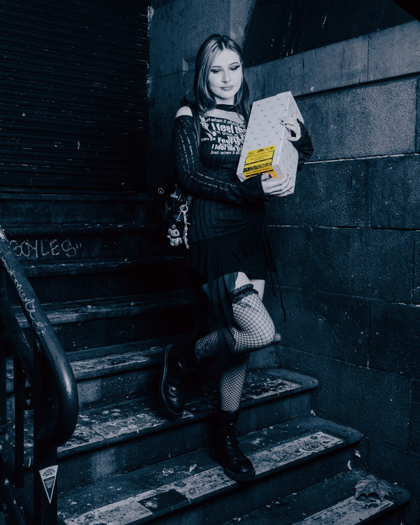 A woman stepping down the stairs with a packaged Shotties™ 33 cm Glass Perc Pillar Bong in clear and blue glass from Bong Warehouse