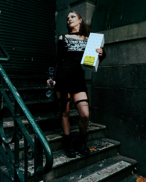 A woman carrying a packaged perk bong alongside a Shotties™ 33 cm Glass Perc Pillar Bong in clear and blue glass from Bong Warehouse