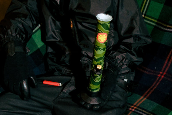 Bong Warehouse Large Tube 33 cm Glass Bong in Camo Sunbaked pattern, steady on a man's palm and a lighter