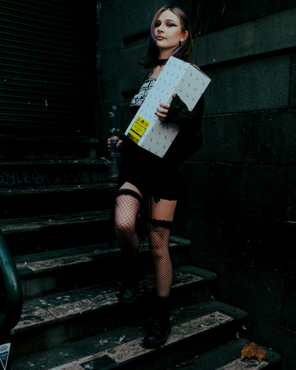 A woman holding the Shotties™ 33 cm Glass Perc Pillar Bong in clear and blue glass from Bong Warehouse on the stairs