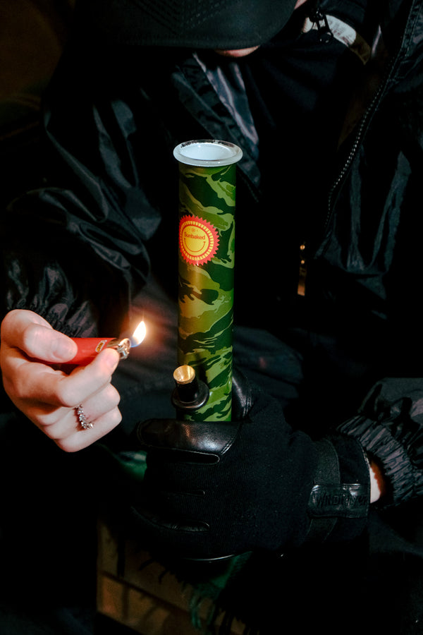 A stoner lighting the Bong Warehouse Large Tube 33 cm Glass Bong in Camo Sunbaked pattern
