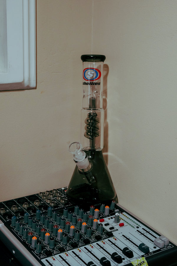 Up-close view of the Shotties™ 30 cm Spiral Perk Glass Beaker Bong in clear and smokey glass from Bong Warehouse on top of the mixing console