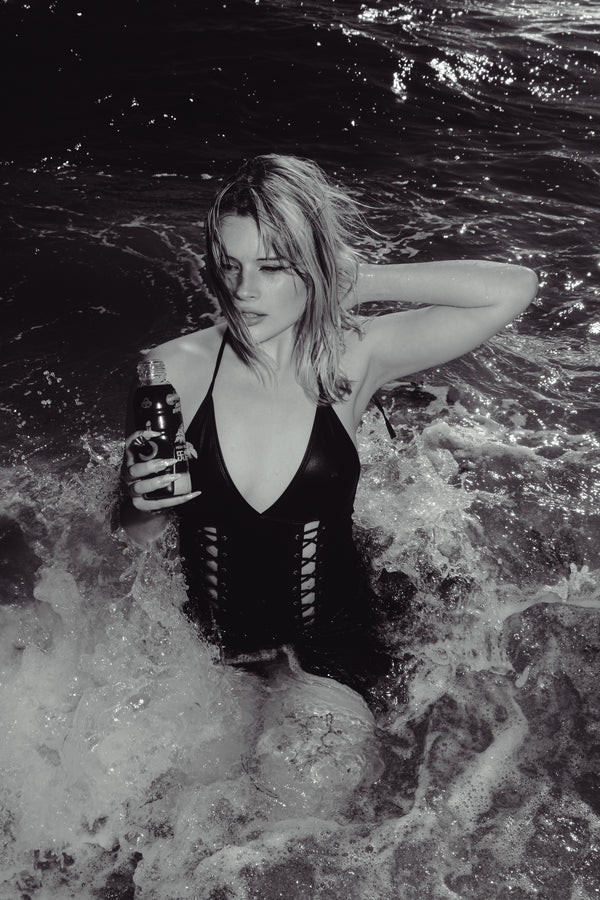 A woman in waves holding a Bong Warehouse Black High Tiger 17.5cm Bottle Bong