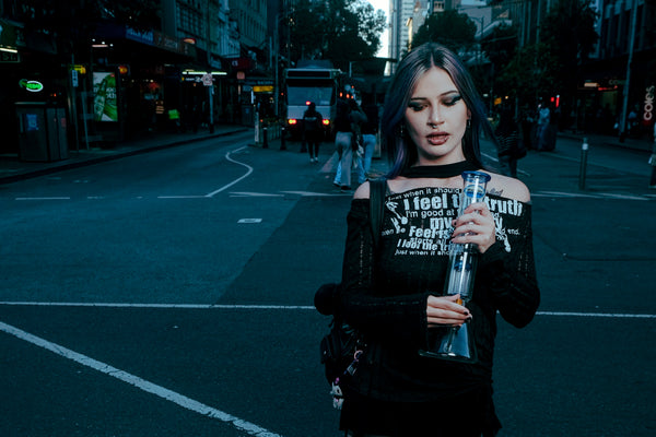 A woman holding the Shotties™ 33 cm Glass Perc Pillar Bong in clear and blue glass from Bong Warehouse in the street