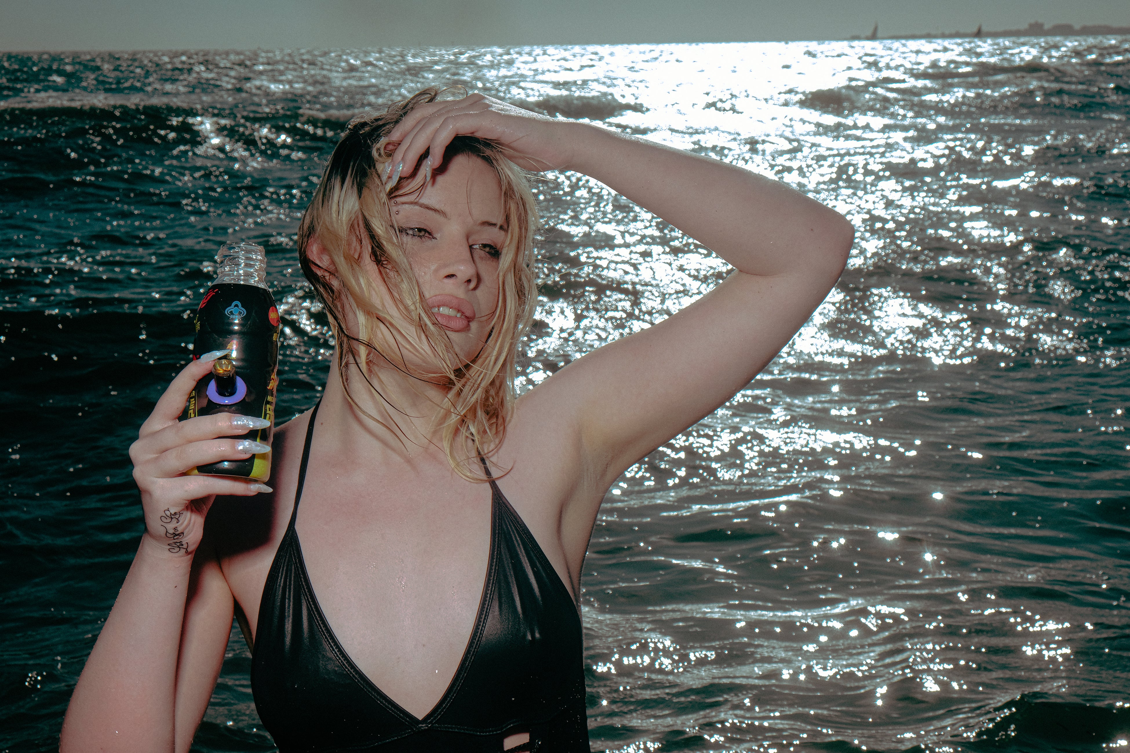A woman standing by the sea holding a Bong Warehouse Black High Tiger 17.5cm Bottle Bong