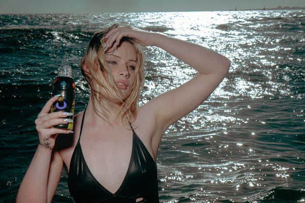 A woman standing by the sea holding a Bong Warehouse Black High Tiger 17.5cm Bottle Bong