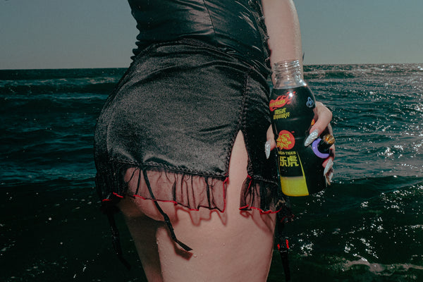 Woman in sexy pose holding Bong Warehouse Black High Tiger 17.5cm Bottle Bong by the seashore, showing metal cone piece