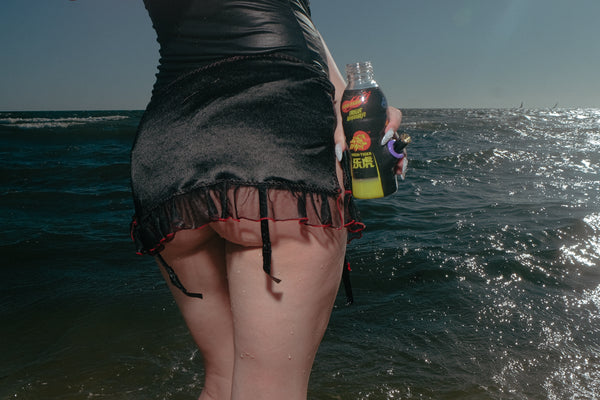 Woman in sexy pose holding Bong Warehouse Black High Tiger 17.5cm Bottle Bong by the seashore.