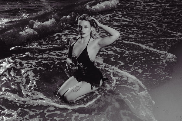 Woman seductively seated at the seashore holding Bong Warehouse Black High Tiger 17.5cm Bottle Bong