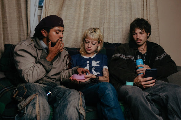 Three people sitting on a couch, looking at a phone  while smoking through Bong Warehouse blue mini bottle bong