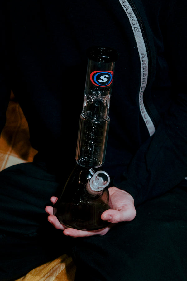 Shotties™ 30 cm Spiral Perk Glass Beaker Bong in clear and smokey glass from Bong Warehouse, on a man's palm