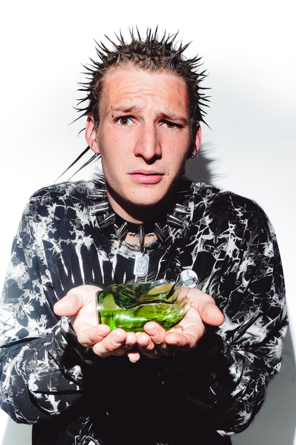 A confused man with the green shattered Bong Warehouse Cute Soda Can Glass Bong resting on his palm