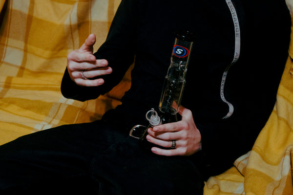 A man holding the Shotties™ 30 cm Spiral Perk Glass Beaker Bong in clear and smokey glass from Bong Warehouse while talking